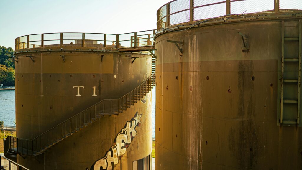 Close-up view of large industrial storage tanks with graffiti under sunny skies.